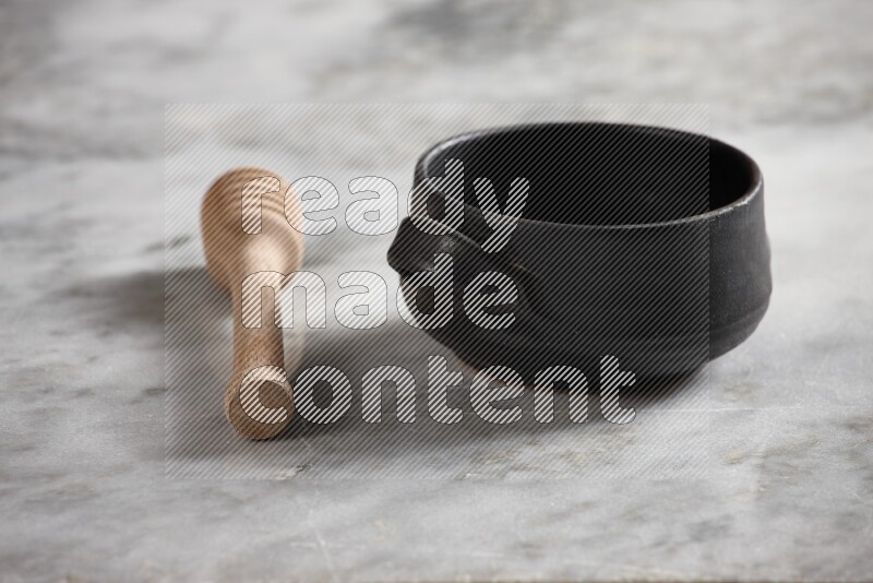 Black pottery bowl with wooden honey dipper on the side on grey marble background
