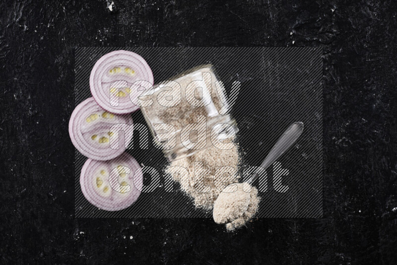 A glass jar full of onion powder flipped with some spilling powder on black background