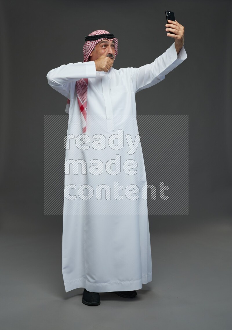 Saudi man with shomag Standing taking selfie on gray background