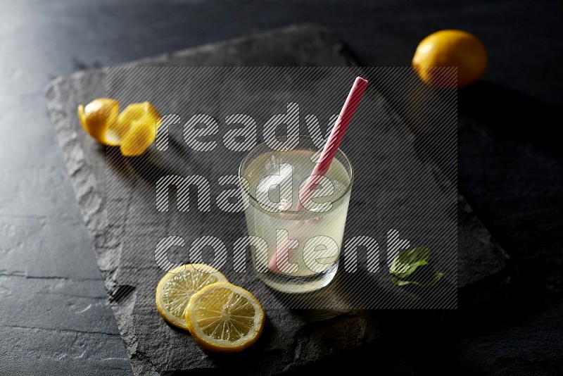 A glass of lemon juice with a straw on black background