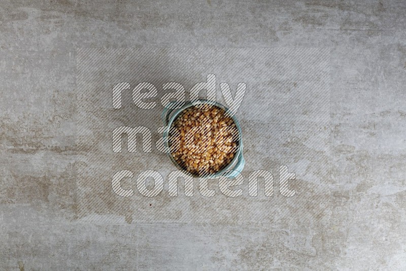 corn kernel in a multi-colored handheld ceramic bowl on a grey textured countertop