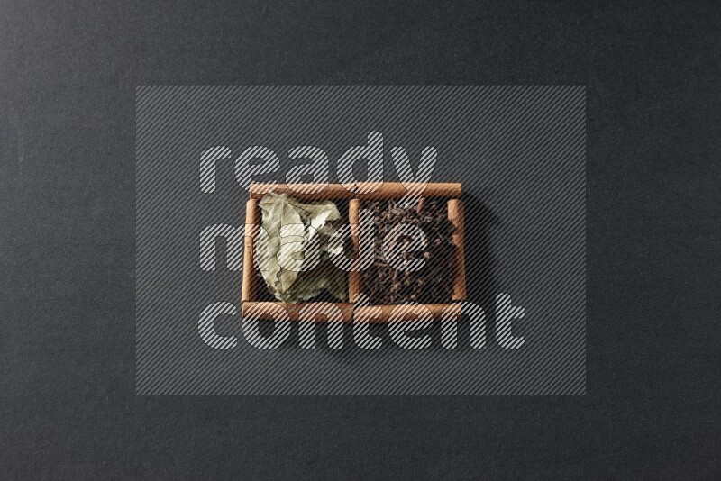 مربعان من أعواد القرفة ممتلئان بالقرنفل وأوراق الغار علي خلفية سوداء