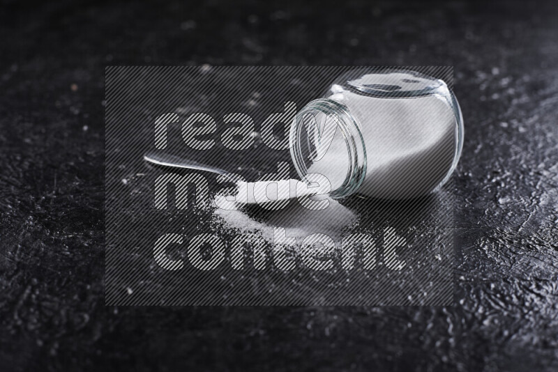 A glass jar full of fine table salt on black background