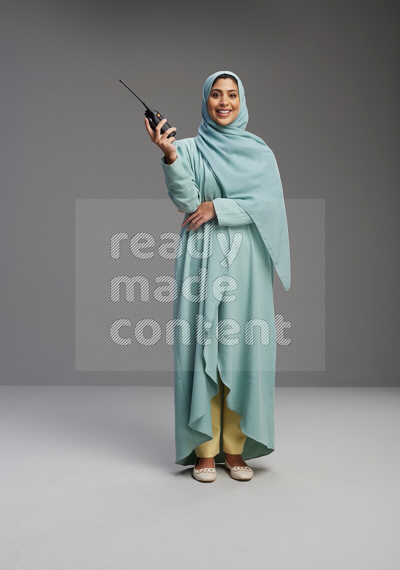 Saudi Woman wearing Abaya standing holding walkie-talkie on Gray background