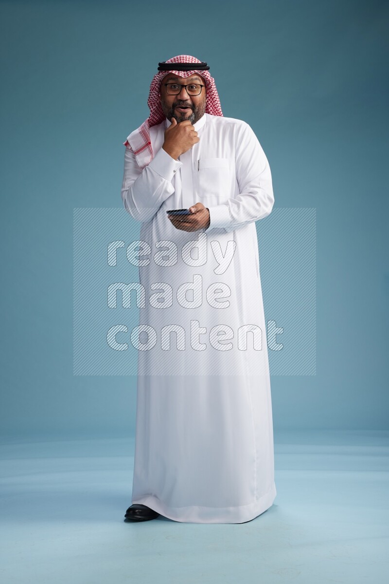 Saudi Man with shimag Standing texting on phone on blue background