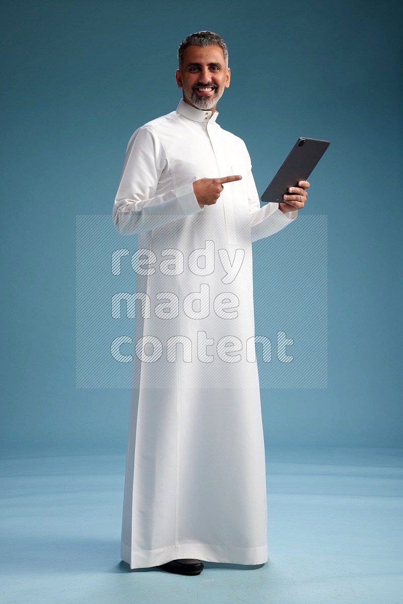Saudi man waring thob with tablet on blue background
