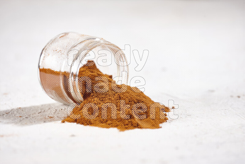 A glass jar full of ground paprika powder flipped with some spilling powder on white background