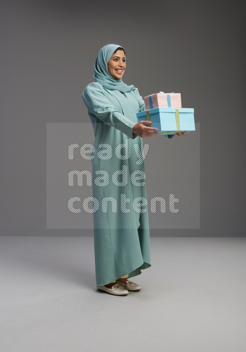 Saudi Woman wearing Abaya standing holding gift box on Gray background