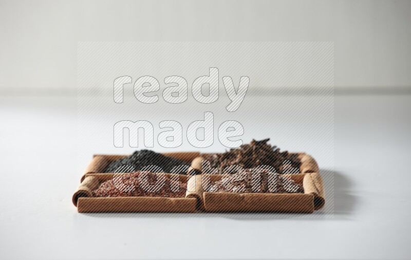 4 مربعات من أعواد القرفة ممتلئة بحبة البركة والقرنفل وبذور الكتان وحب الرشاد على أرضية بيضاء