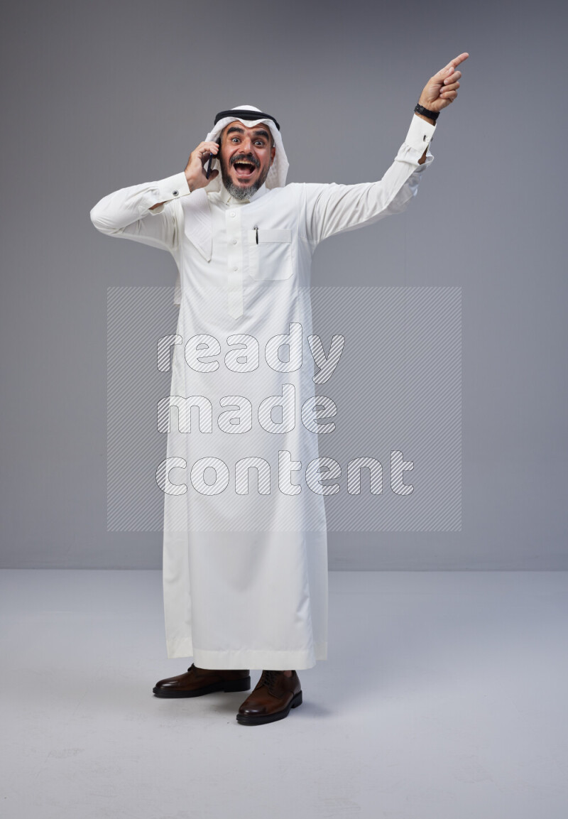 Saudi man Wearing Thob and white Shomag standing talking on phone on Gray background