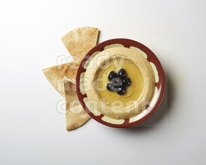 Hummus in a traditional plate garnished with black olives on a white background