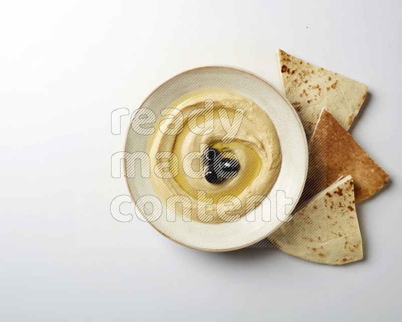 Hummus in a pottry plate garnished with black olives on a white background