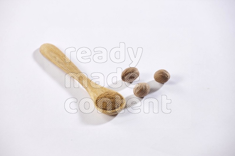 A wooden spoon full of nutmeg powder with whole nutmeg seeds beside it on a white flooring