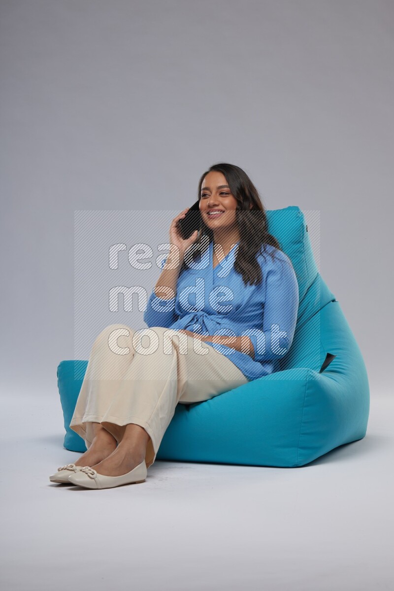 A woman sitting on a blue beanbag and talking on the phone