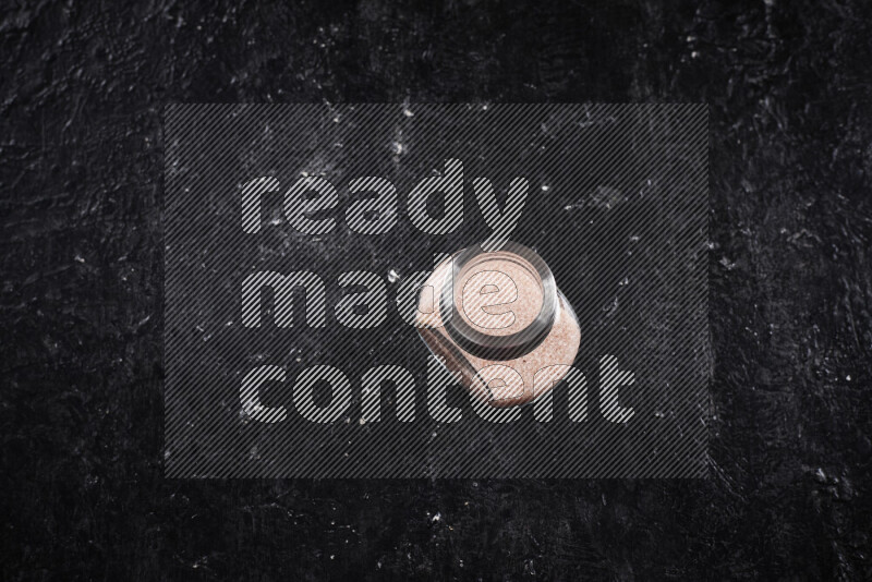 A glass jar full of fine himalayan salt on black background