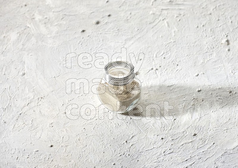 Herbal Glass jar full of white pepper powder on textured white flooring