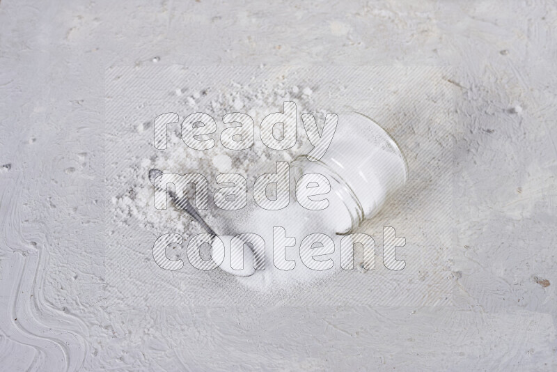 A glass jar full of table salt with some sea salt crystals beside it on a white background