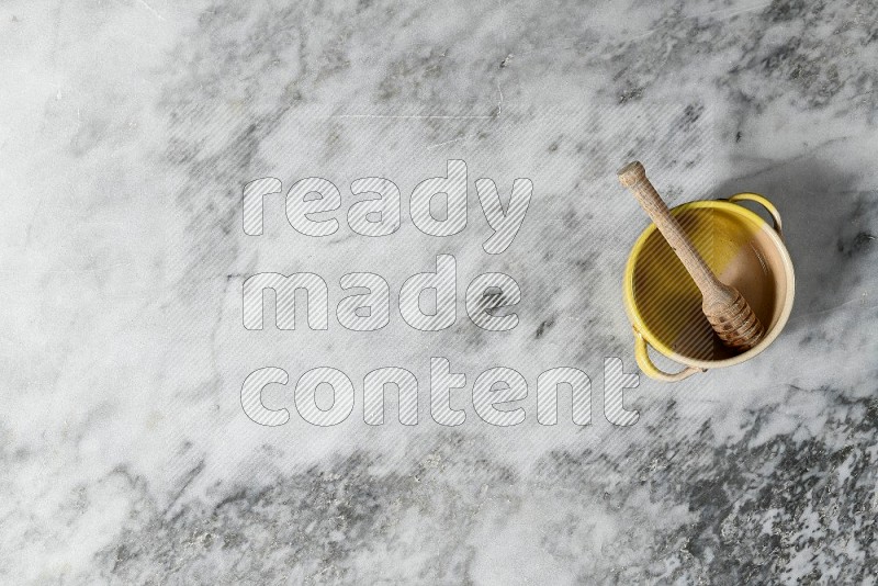 Multicolored Pottery Bowl with wooden honey handle in it, on grey marble flooring, Top View