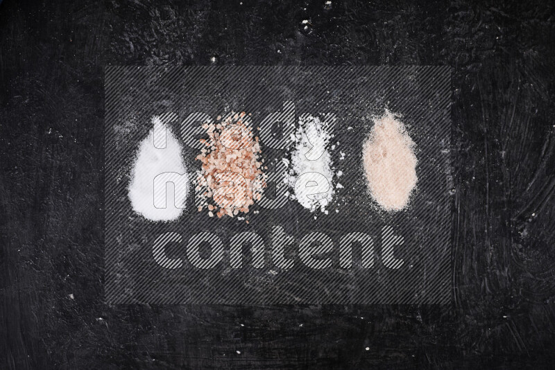 4 glass jars filled with table salt, coarse sea salt, fine himalayan salt and coarse himalayan salt on black background