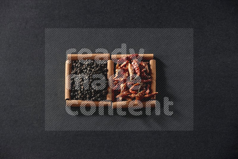 2 squares of cinnamon sticks full of chilis and black peppers on black flooring