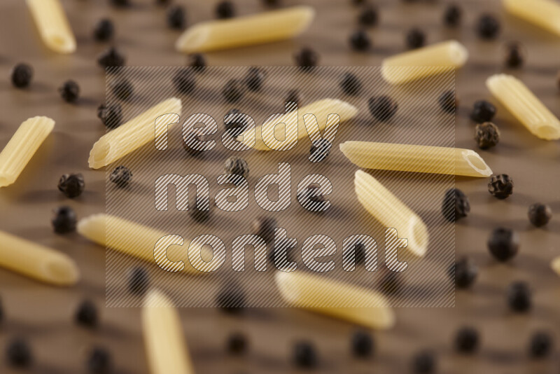 Raw pasta with different ingredients such as cherry tomatoes, garlic, onions, red chilis, black pepper, white pepper, bay laurel leaves, rosemary and cardamom on beige background