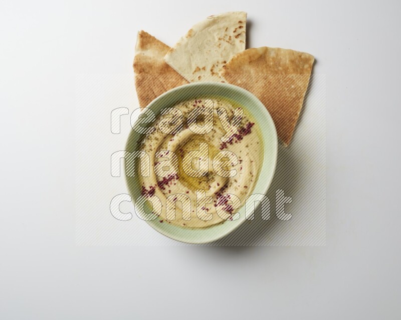 Hummus in a green plate garnished with zattar & sumak on a white background