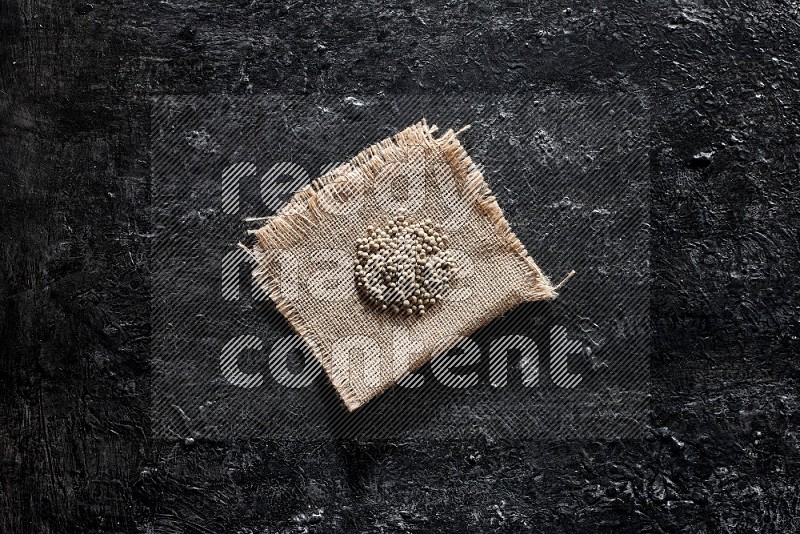 White pepper beads on a burlap piece of fabric on textured black flooring
