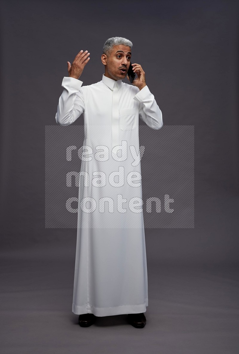 Saudi man wearing thob standing talking on phone on gray background