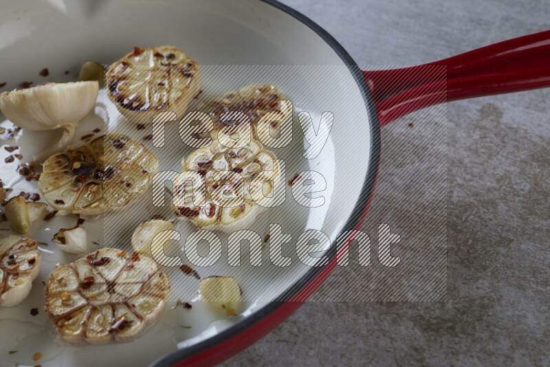 half's roasted garlic in a red-coated cast iron pan on a grey textured countertop