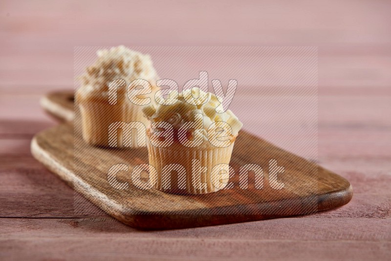 Vanilla mini cupcake topped with white chocolate curls on a wooden board