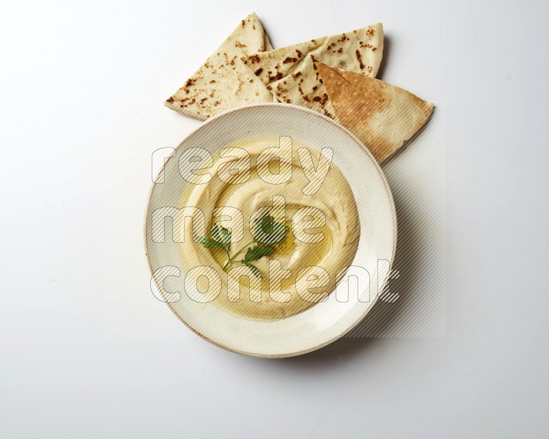 Hummus in a pottry plate garnished with parsley on a white back ground