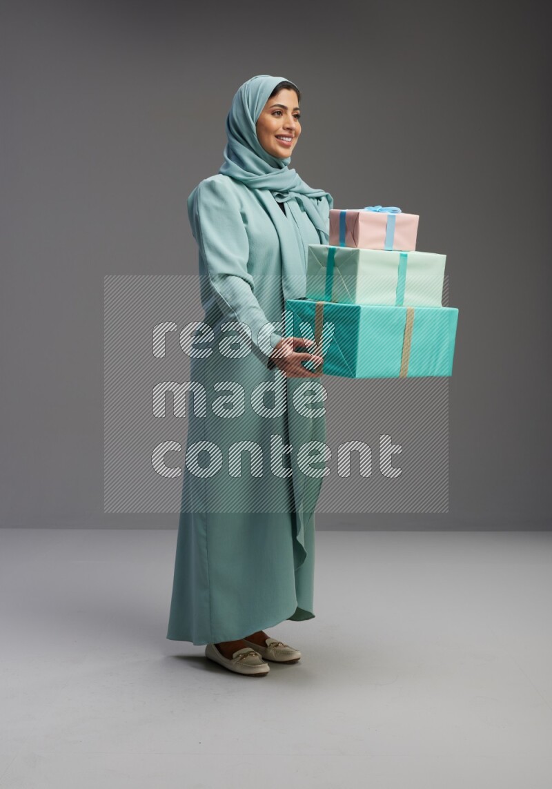 Saudi Woman wearing Abaya standing holding gift box on Gray background