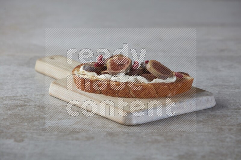 figs slices  with cream cheese on toasted sourdough slice on a wooden board on textured grey background