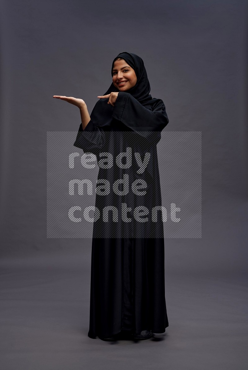 Saudi woman wearing Abaya standing interacting with the camera on gray background