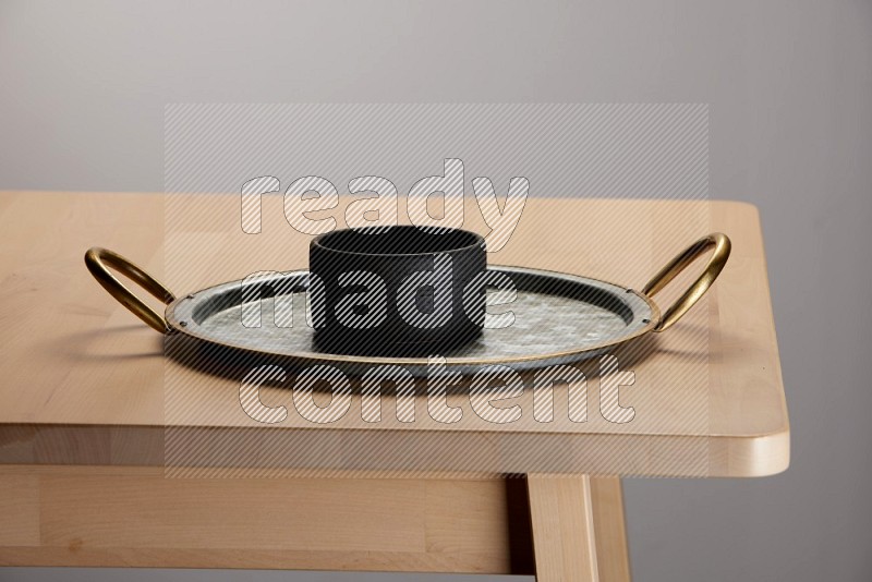 black bowl placed on a rounded stainless steel tray with golden handels on the edge of wooden table