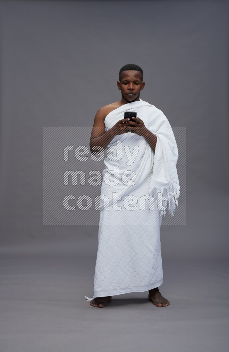 A man wearing Ehram Standing texting on phone on gray background
