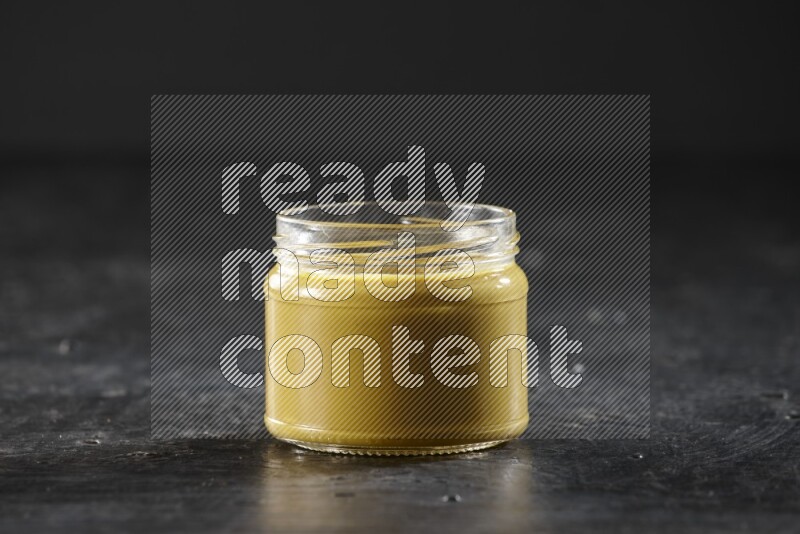 A glass jar full of mustard paste on a textured black flooring