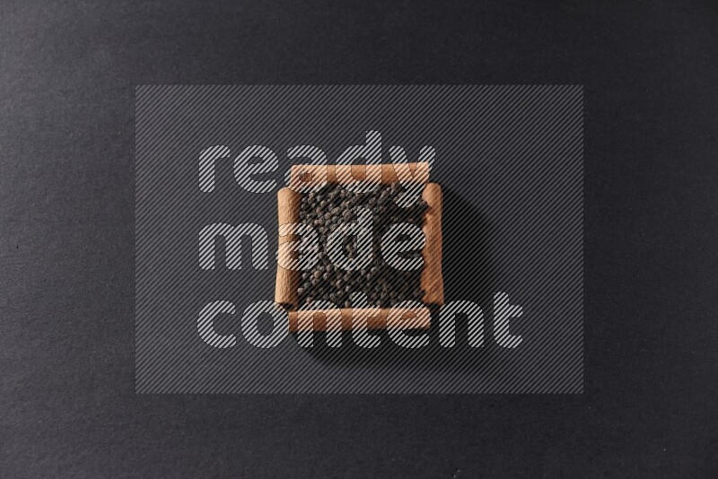 A single square of cinnamon sticks full of black pepper on black flooring