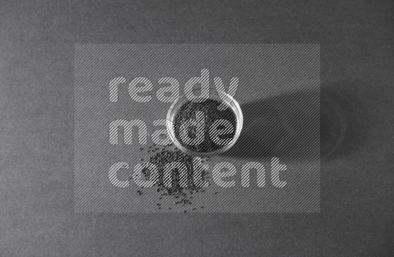 وعاء زجاجي ممتلئ ببذور حبة البركة مع بعض البذور بجانبه علي خلفية سوداء