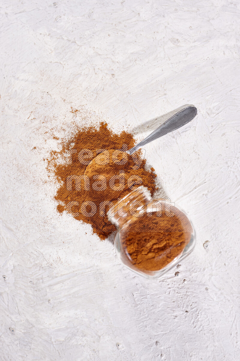 A glass jar full of ground paprika powder flipped with some spilling powder on white background