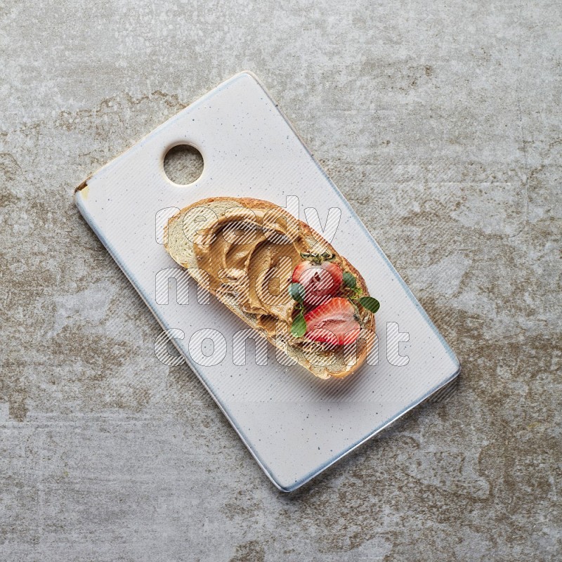 open faced peanut butter sandwich with strawberries on a grey textured background