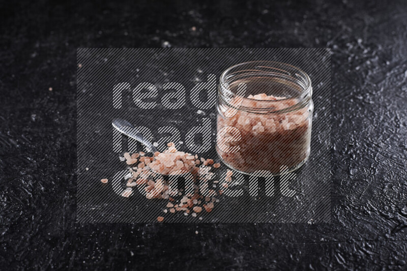 A glass jar full of coarse himalayan salt crystals on black background