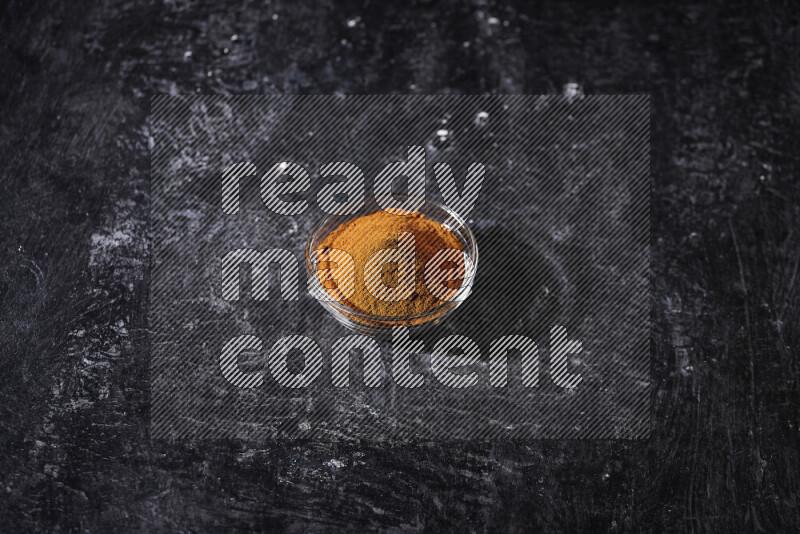 A glass bowl full of ground paprika powder on black background