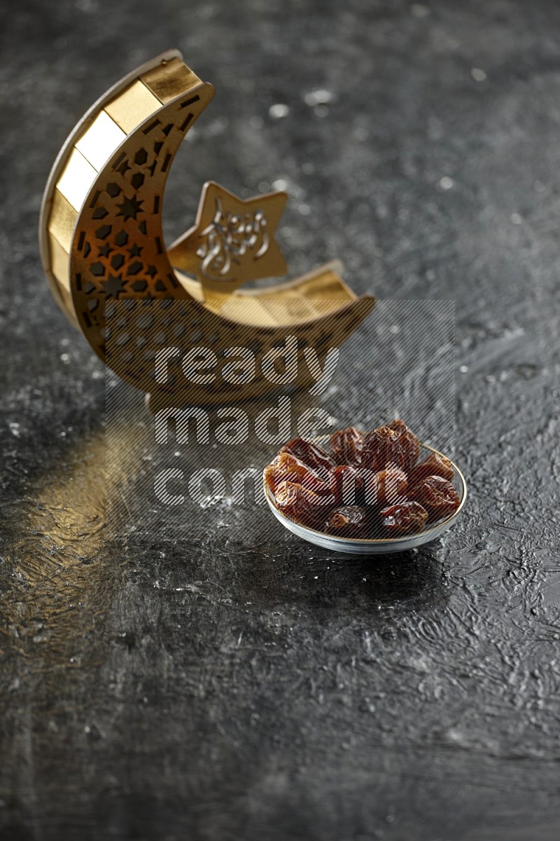 A wooden golden crescent lantern with different drinks, dates, nuts, prayer beads and quran on textured black background