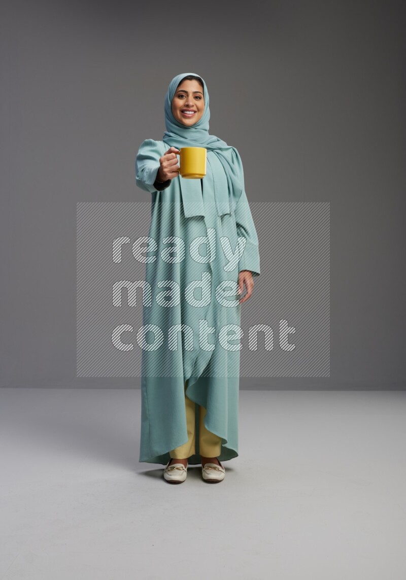 Saudi Woman wearing Abaya standing  holding a mug on Gray background