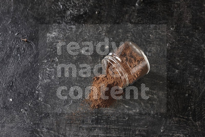 A flipped glass jar full of cloves powder on a textured black flooring