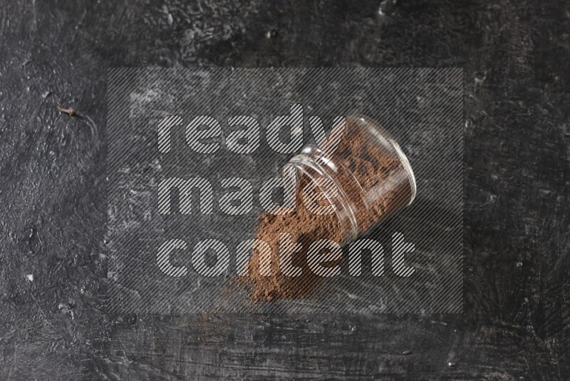 A flipped glass jar full of cloves powder on a textured black flooring
