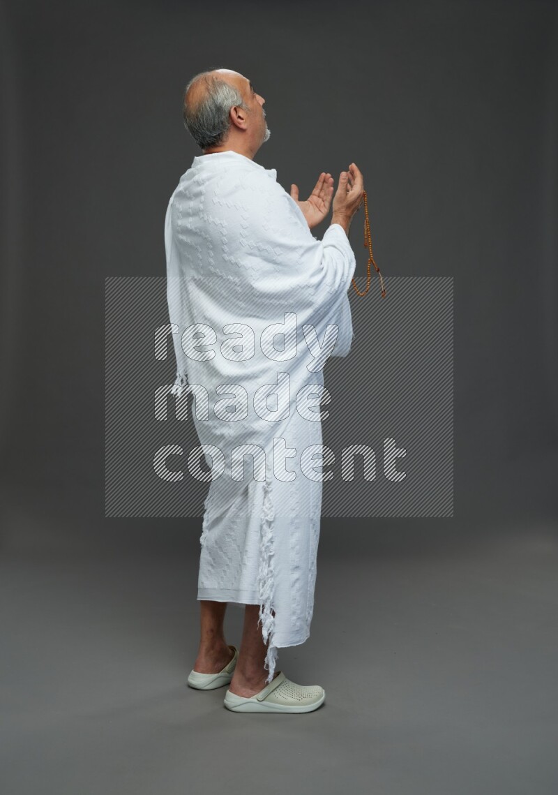 A man wearing Ehram Standing dua'a on gray background