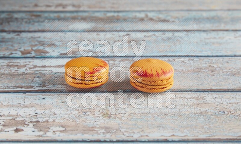 45º Shot of two orange Exotic macarons on light blue wooden background