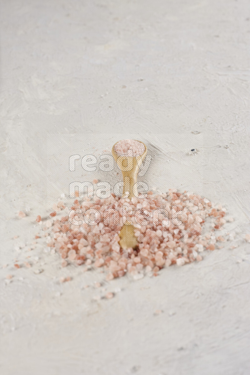 A wooden spoon full of pink himalayan salt on white background